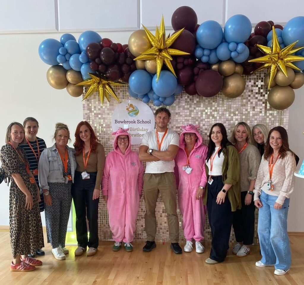 Male and female staff under a balloon arch at a birthday party